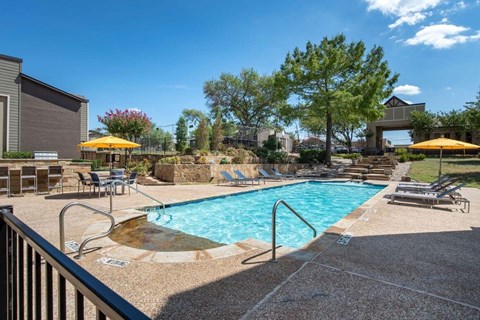 our resort style swimming pool is surrounded by lounge chairs and umbrellas
