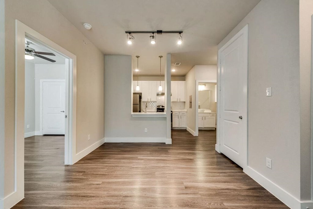 an empty living room with a kitchen in the background
