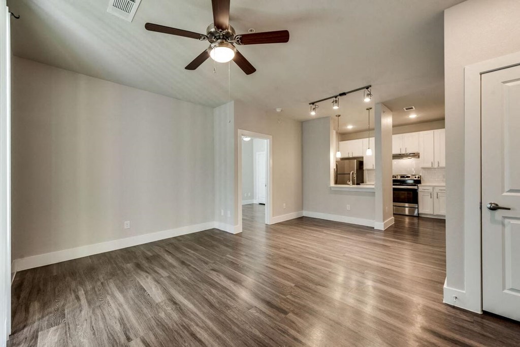 an empty living room with a ceiling fan and a kitchen