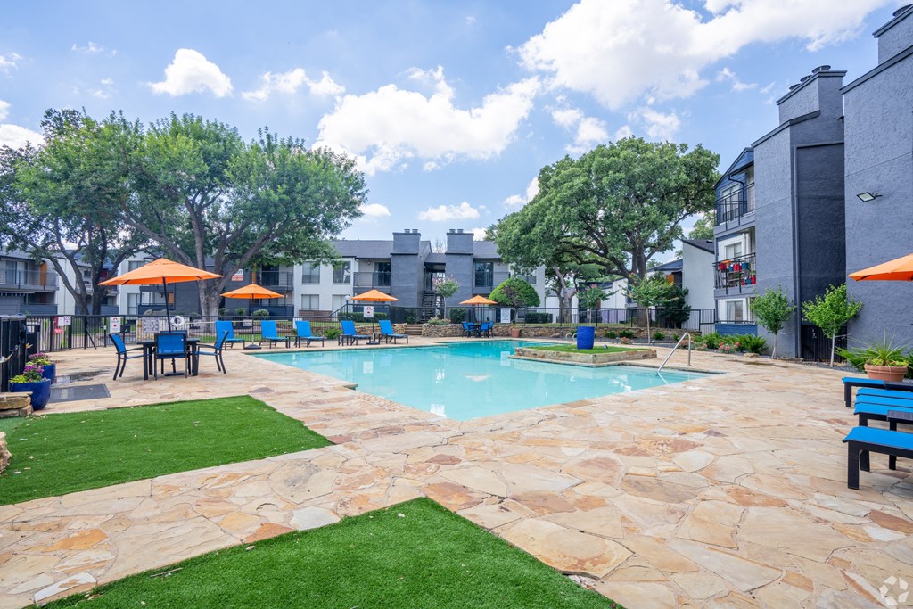 a swimming pool with tables and umbrellas in front of a building at District 2308, Arlington Texas?