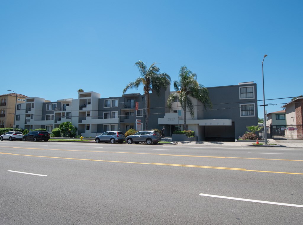 an apartment building with palm trees in front of it on a city street