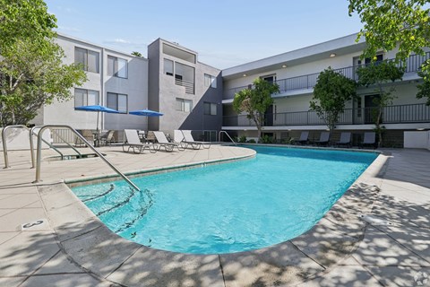A swimming pool in front of a building with a blue umbrella.