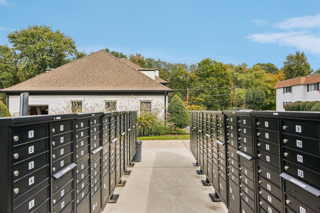 A series of black mailboxes are lined up on a sidewalk in front of a white house.