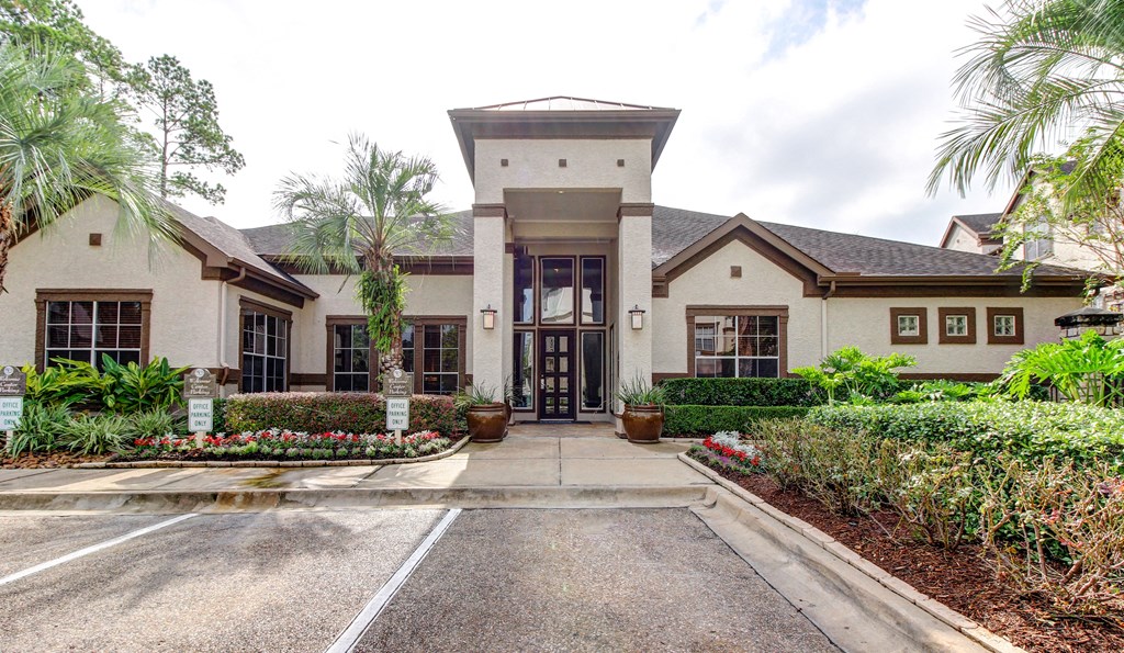 the front entrance of an apartment clubhouse with a driveway and plants at Stone Creek at Old Farm Apartments, Houston