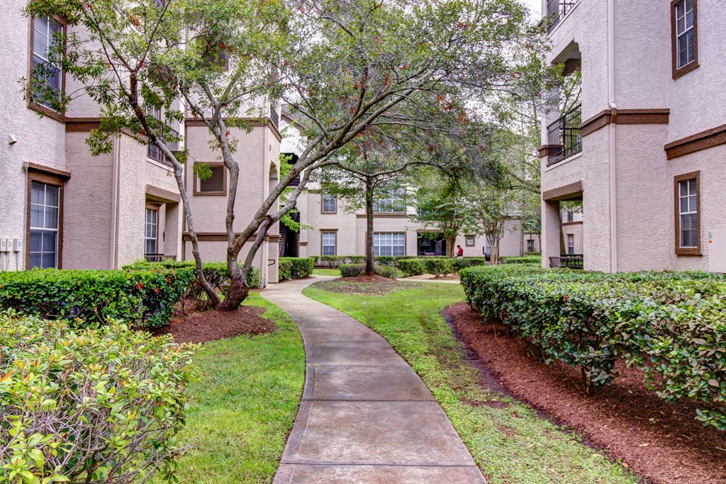 a sidewalk leading to an apartment building with trees and bushes at Stone Creek at Old Farm Apartments, Texas