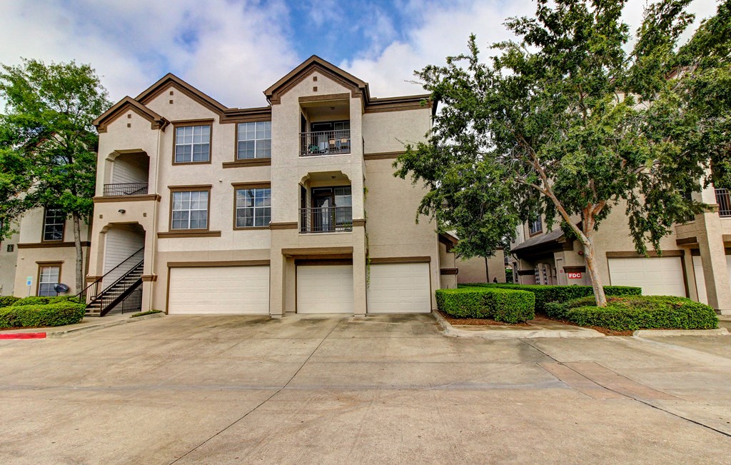 front view of an apartment building with garages and trees at Stone Creek at Old Farm Apartments, Houston, Texas