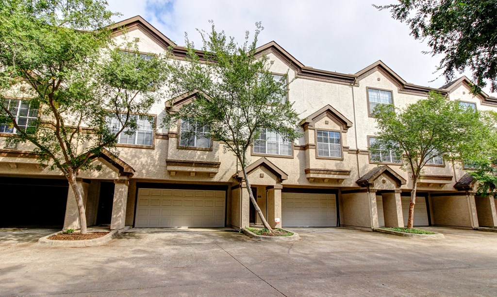 the front of a house with two garages and trees at Stone Creek at Old Farm Apartments, Texas 77063