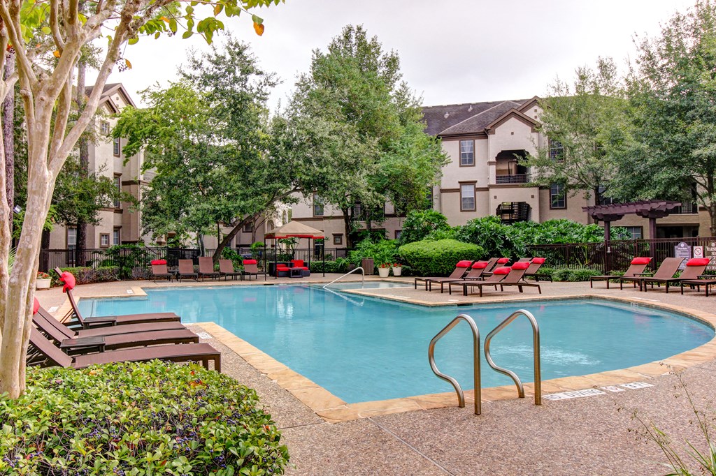 a swimming pool with chairs and trees and an apartment building in the background at Stone Creek at Old Farm Apartments, Houston, TX