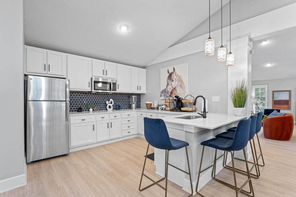 a kitchen with white cabinetry and a large white island with three blue chairs