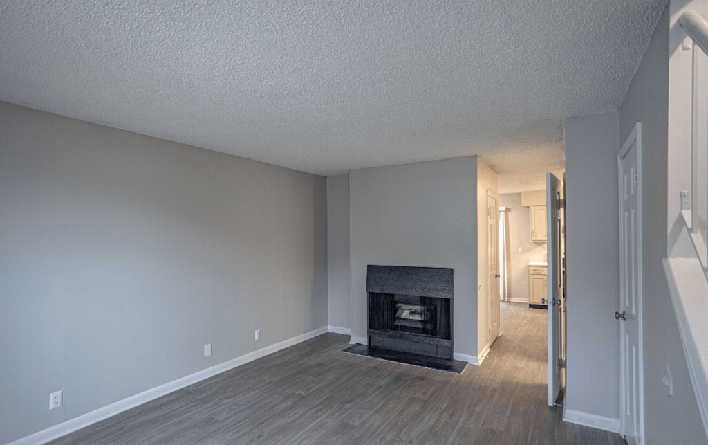an empty living room with a fireplace and a hallway with a door