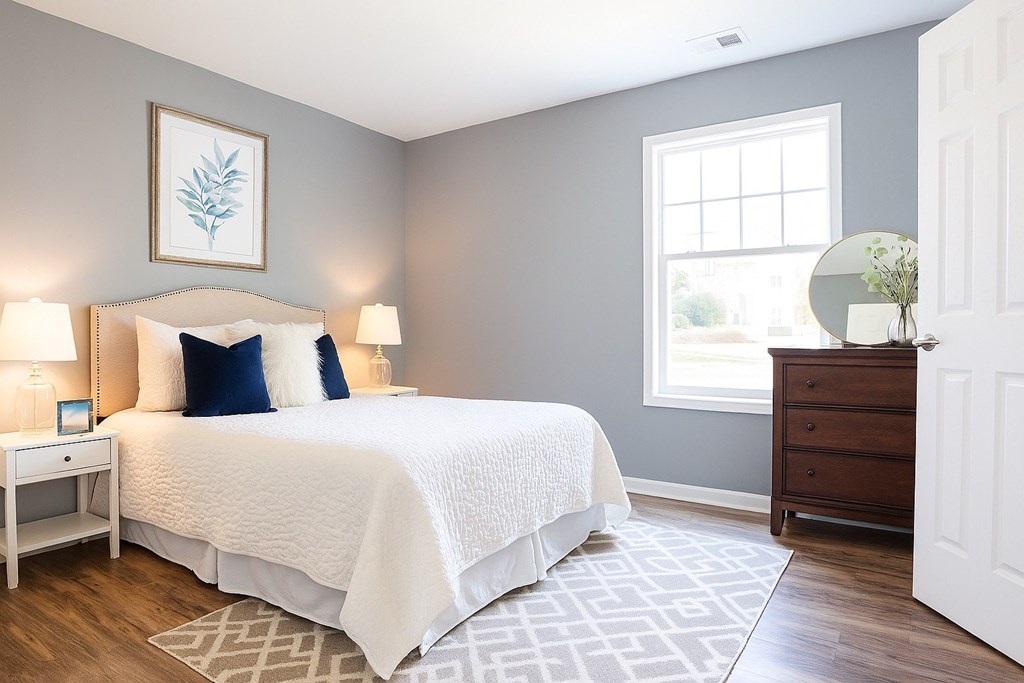 A bedroom with a white bed and a white nightstand with a lamp.