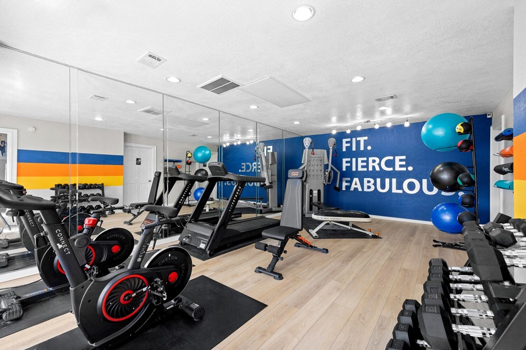 a gym with cardio machines and weights on the floor and a wall with a quote