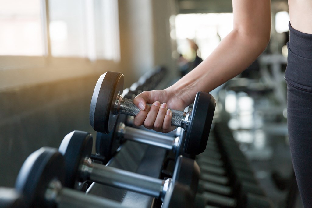 a woman holding dumbbells on a treadmill in a gym