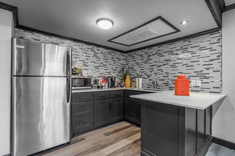 A kitchen with a stainless steel refrigerator and a stone backsplash.