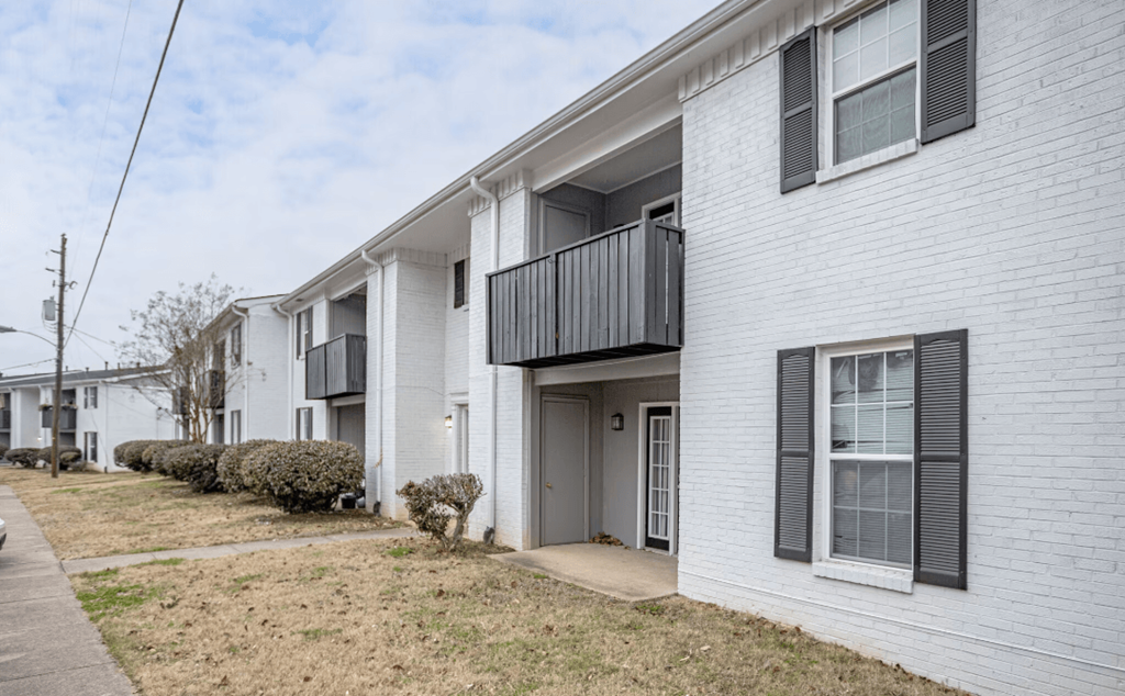 a white brick apartment building with a balcony and a sidewalk
