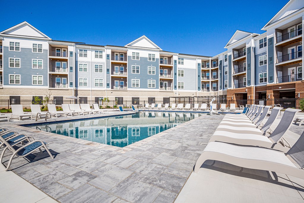 an outdoor pool with lounge chairs and an apartment building in the background