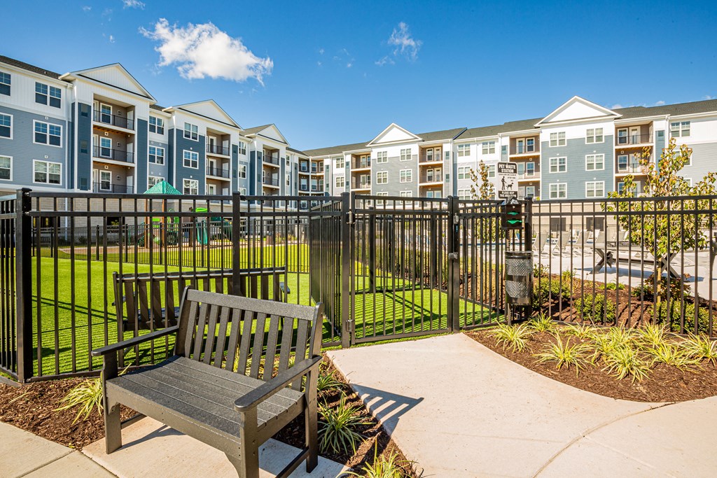 an empty bench sits in front of a fenced in yard with an apartment building