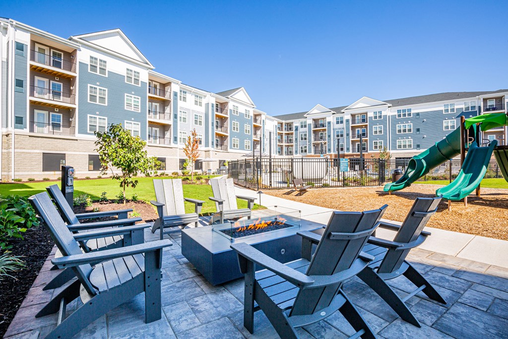 an outdoor patio with a firepit and chairs at an apartment complex with a playground