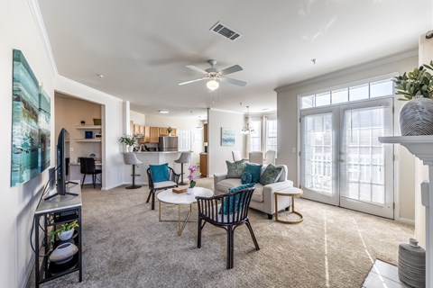 A living room with a grey carpet and a white ceiling fan.