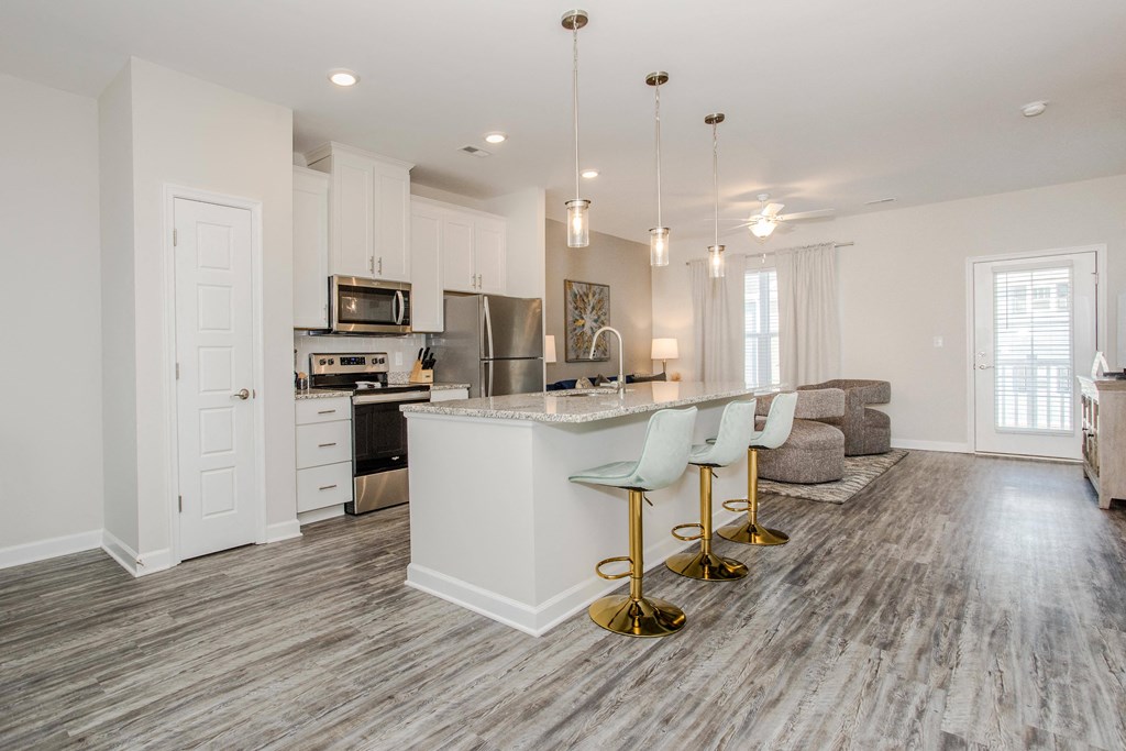 an open kitchen and living room with white cabinets and a marble counter top