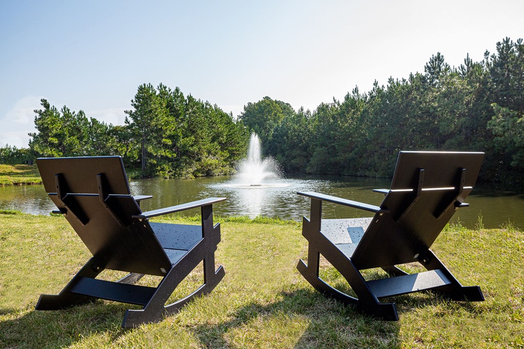 two wooden chairs in front of a pond with a fountain