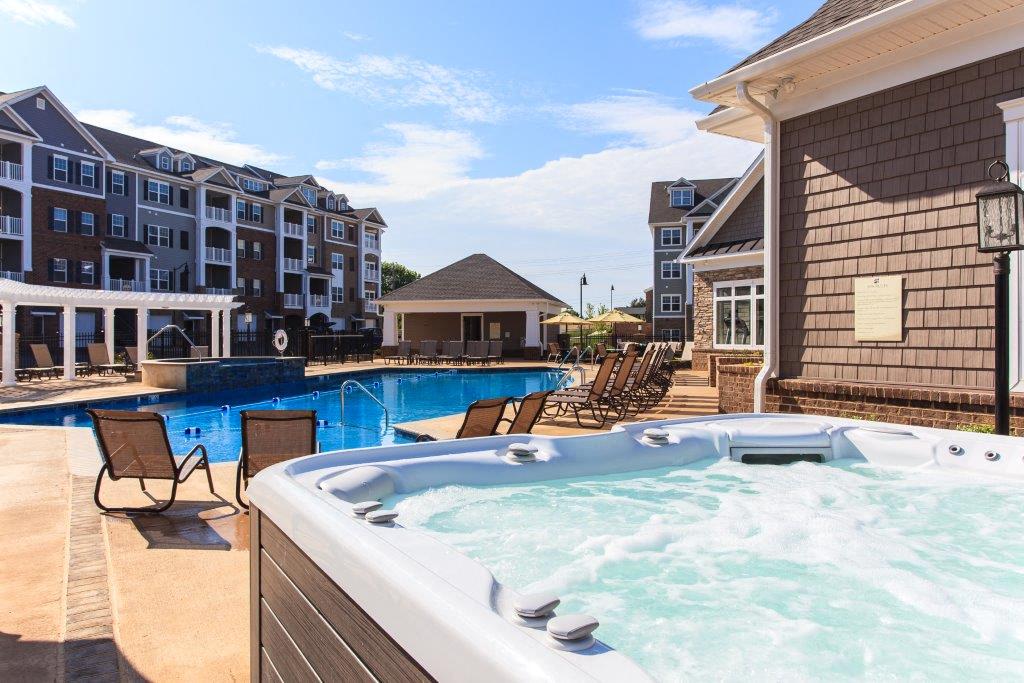 a pool with a jacuzzi and chairs next to an apartment building