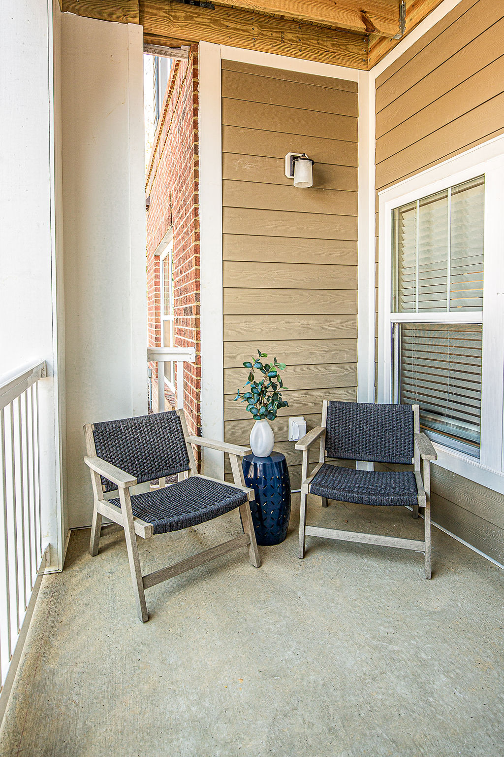a porch with two chairs and a vase with a plant on it