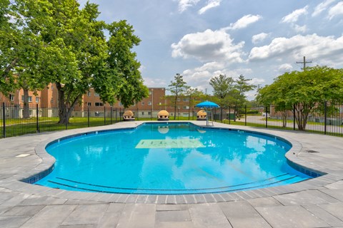A round blue swimming pool surrounded by a black fence and trees.