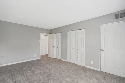 A room with grey walls and carpeted floor with three white doors.