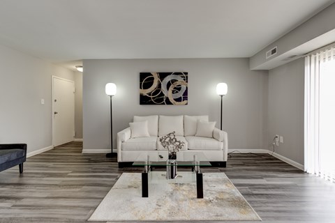 A modern living room with a white couch and a large abstract painting on the wall.