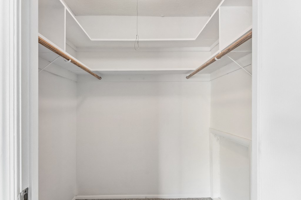 an empty room with white walls and a white closet with wooden rods on the ceiling