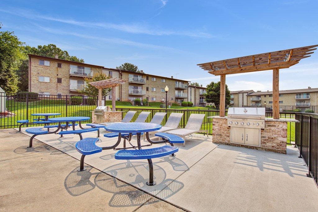 a patio with picnic tables and a grill in front of an apartment building