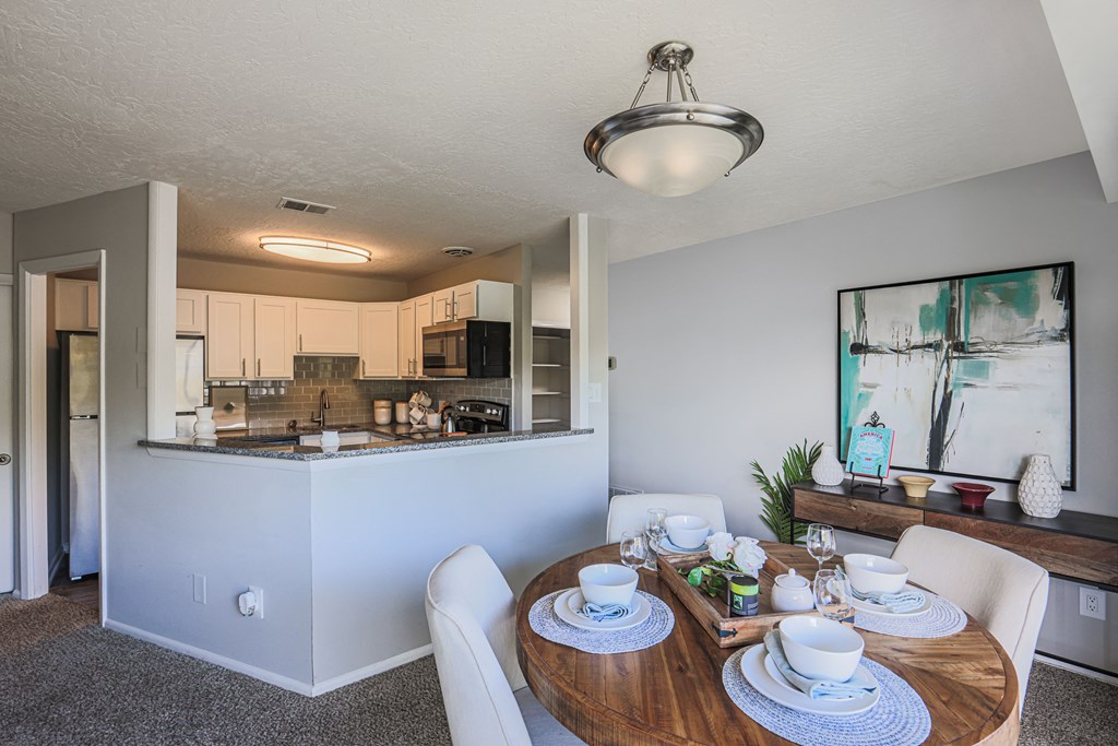 a dining area with a table and chairs and a kitchen in the background