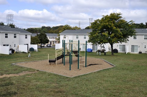 A playground with a swing set and a slide in the middle of a grassy area.