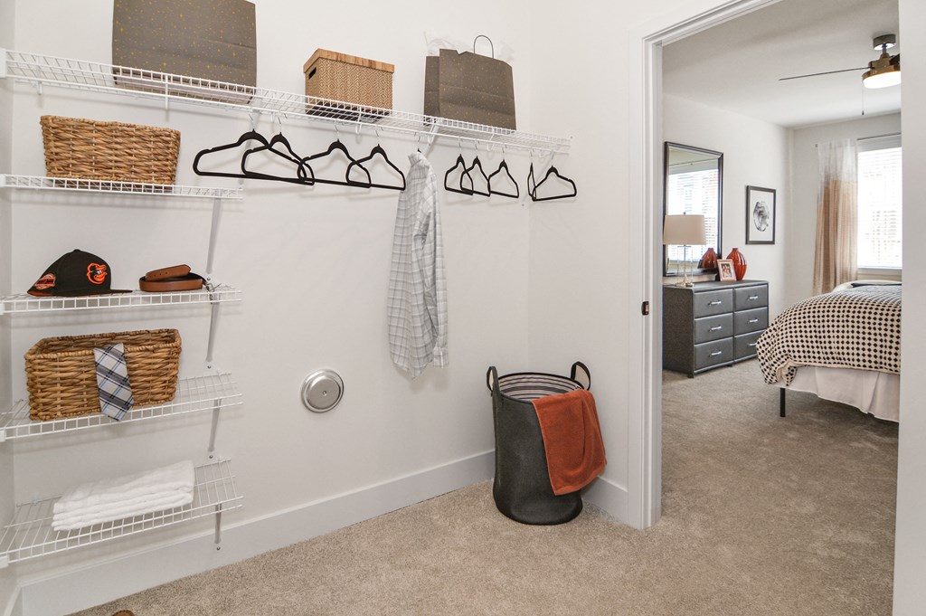 a walk in closet in a bedroom with a bed and a dresser in the background