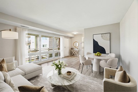 A modern living room with a large window, a white sofa, a coffee table, and a painting on the wall.