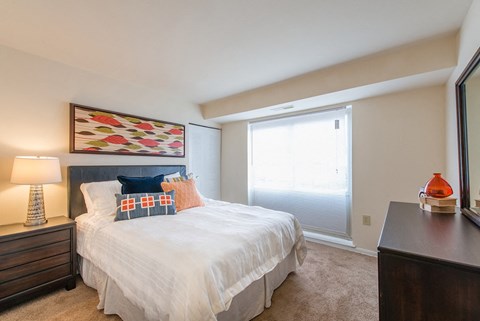 A bedroom with a bed, nightstand, lamp, and a painting on the wall.