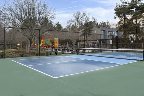 A tennis court with a playground in the background.