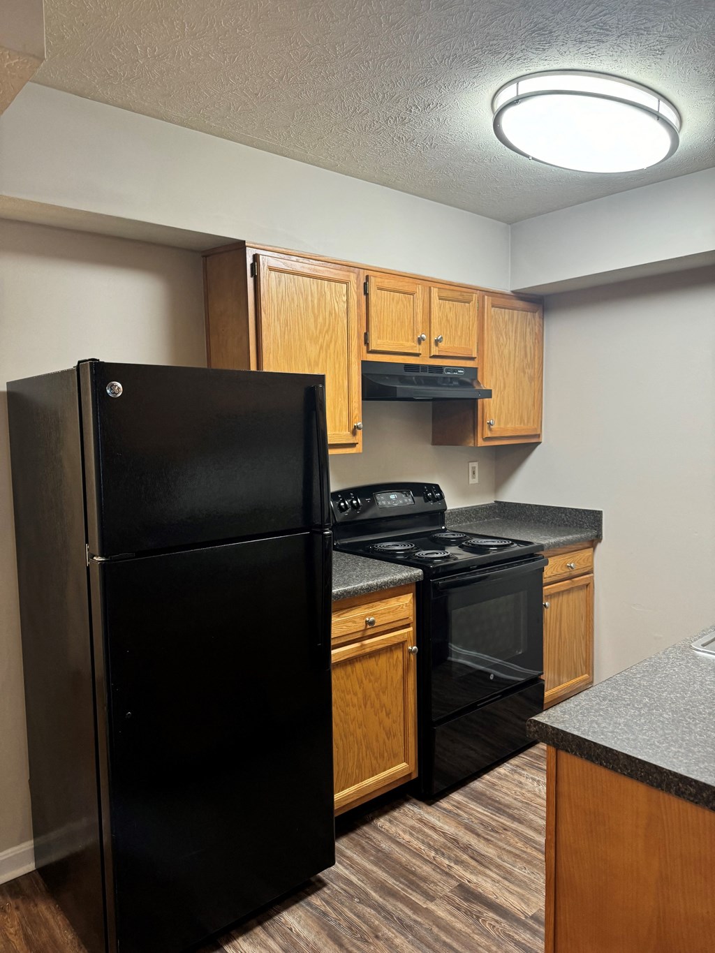 A black refrigerator stands in a kitchen with wooden cabinets and a black stove.