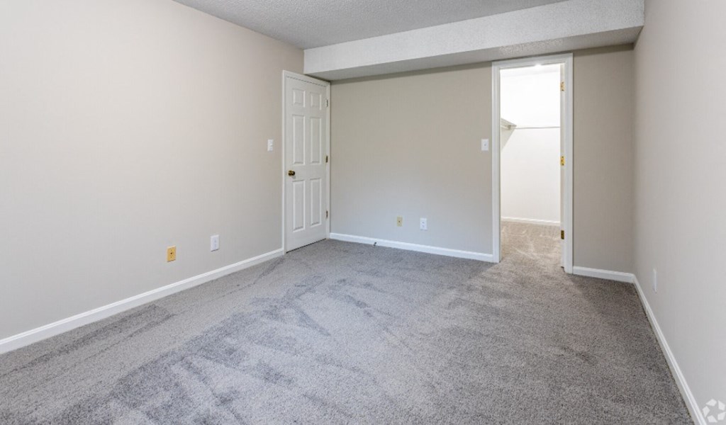 an empty living room with carpet and a door to a bedroom