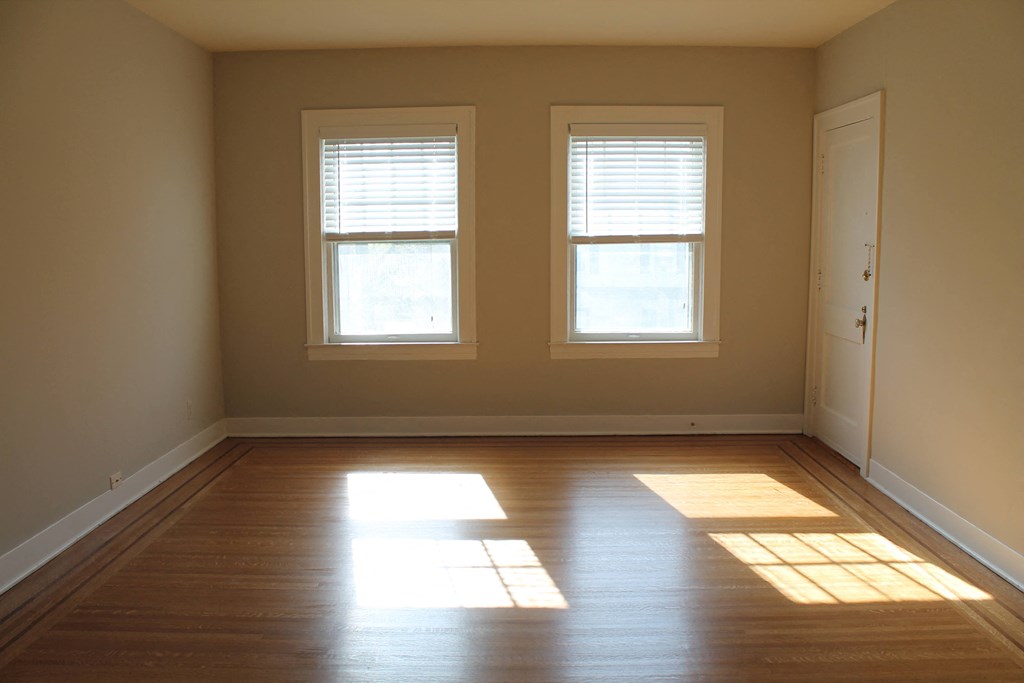 an empty room with two windows and wooden floors