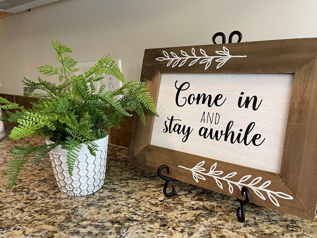 come in and stay awhile sign on a counter with a plant