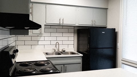 A kitchen with a black stove top oven, a black fridge, and a white counter top.