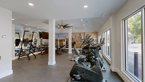 A gym with a row of stationary bikes and a fan.