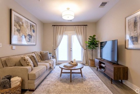 A living room with a beige couch, a wooden coffee table, and a flat-screen TV mounted on the wall.