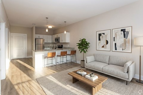 A living room with a grey couch, a coffee table, and a kitchen in the background.