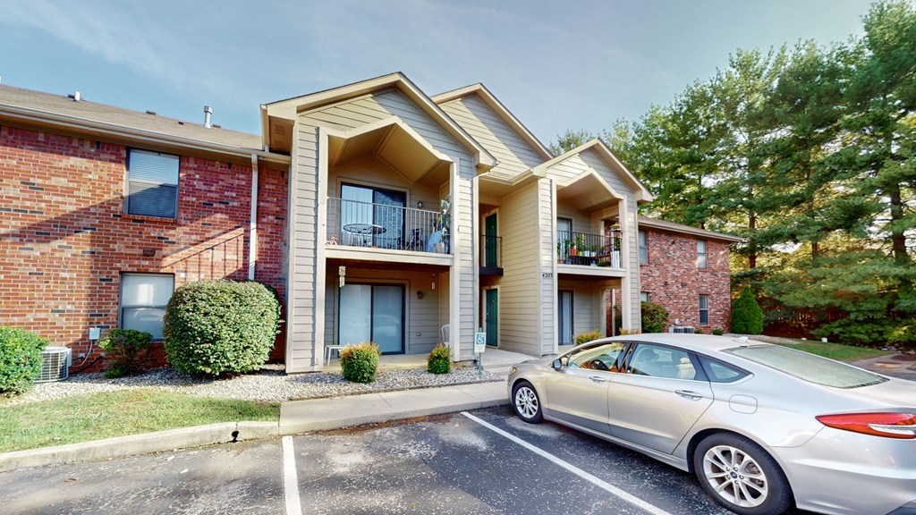 A silver car is parked in front of a two-story apartment building.