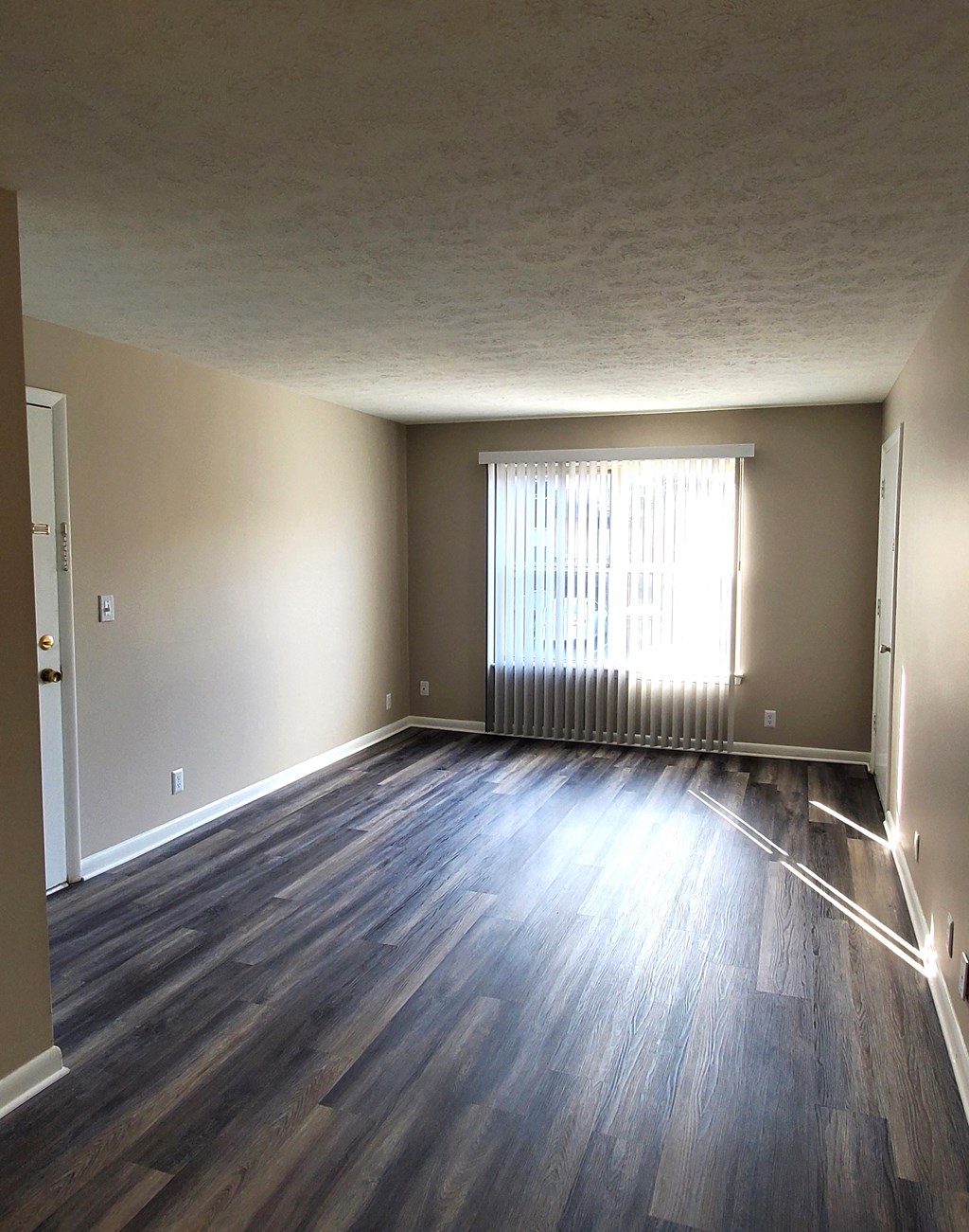 A room with wooden flooring and a window with blinds.