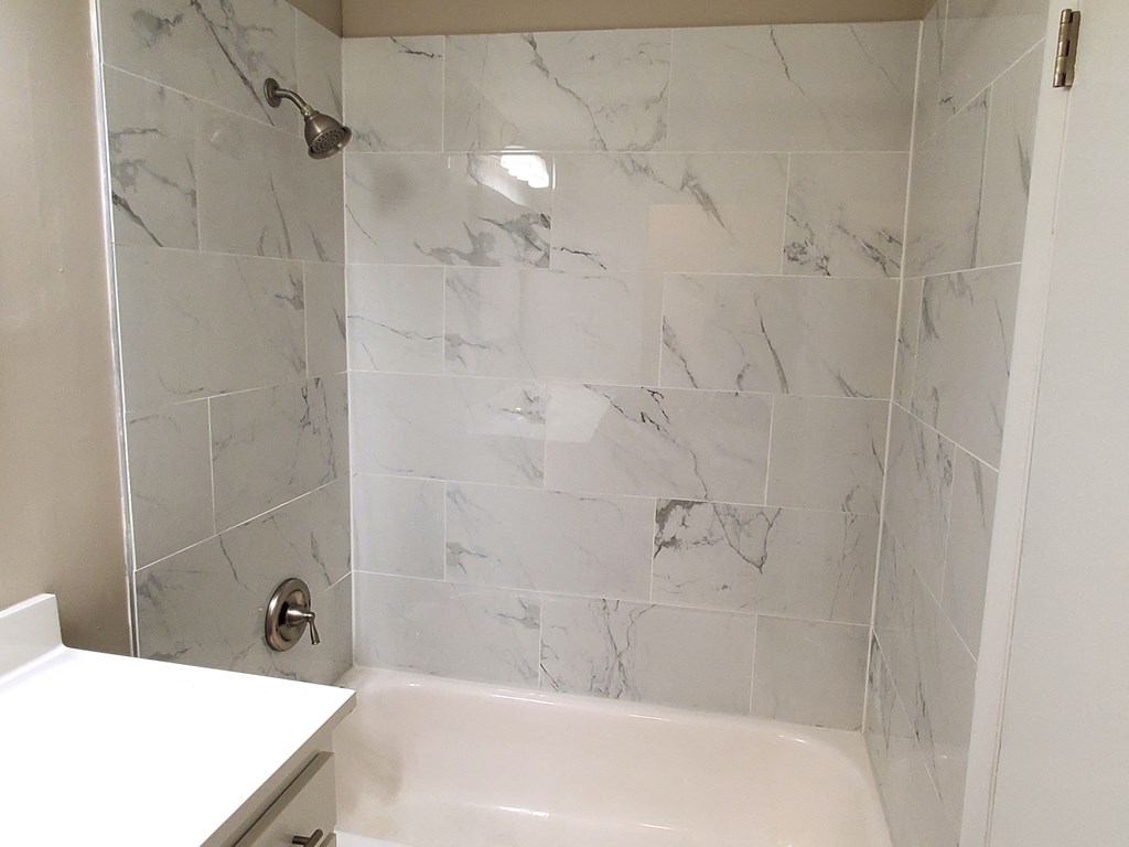 A white bathtub sits in a bathroom with marble tiles on the wall.