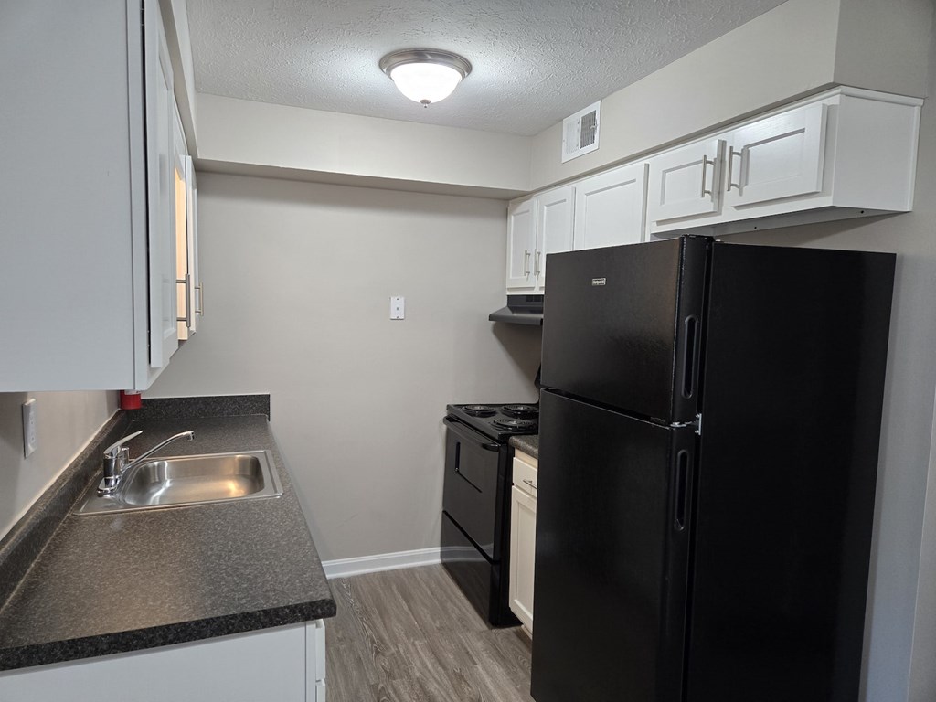 A black refrigerator sits in a kitchen with white cabinets.